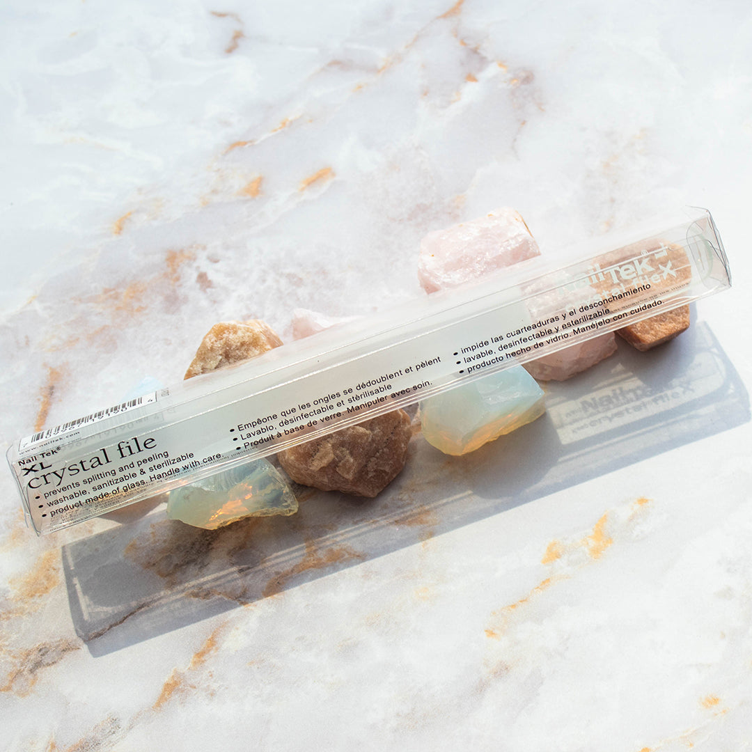Packaged bundle of Nail Tek XL Crystal File 7 inch laid on top of decorative stones on marble background